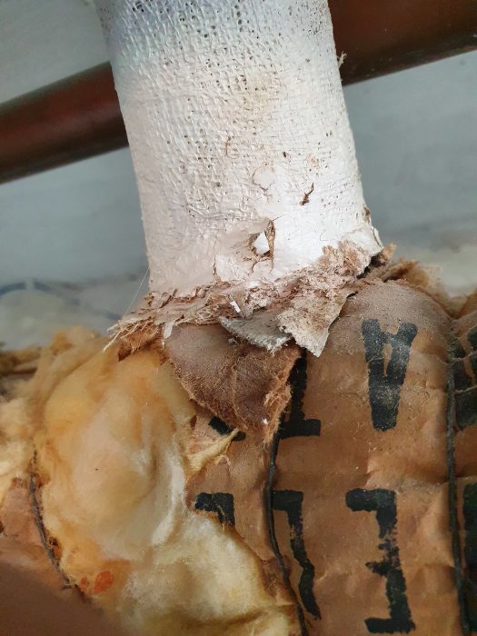 Gamla isolerade rör i källare med skadat isoleringsmaterial som kan innehålla asbest.