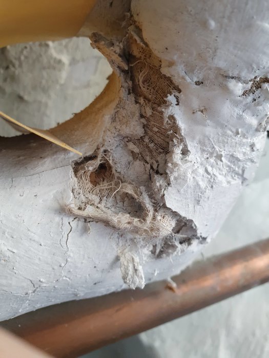 Gamla isolerade rör i källare med synlig fjädrande fiberstruktur som kan vara asbest.