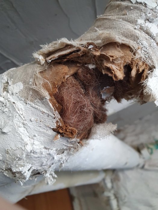 Närbild av gammalt isolerat rör med misstänkt asbest, slitna fibrer och ytskikt.