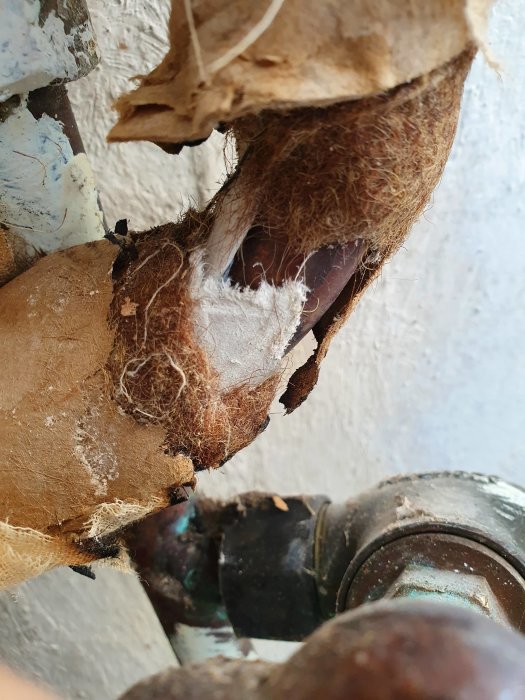 Gamla isolerade rör i källare med fransig, fibrig yta som kan innehålla asbest.