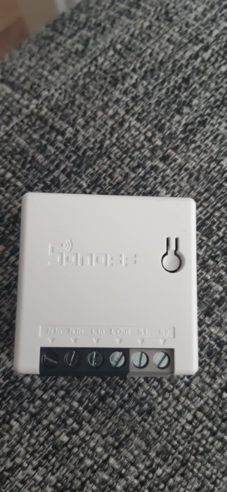 Sonoff Mini smart switch enhet med tydliga etiketter för N, L och S1 S2 terminaler på en texturerad grå bakgrund.