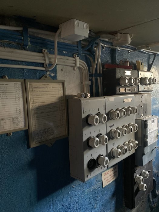 Elektriskt skåp med säkringar, kablar, och mätare på en blå vägg, tecken på skada vid några säkringar.