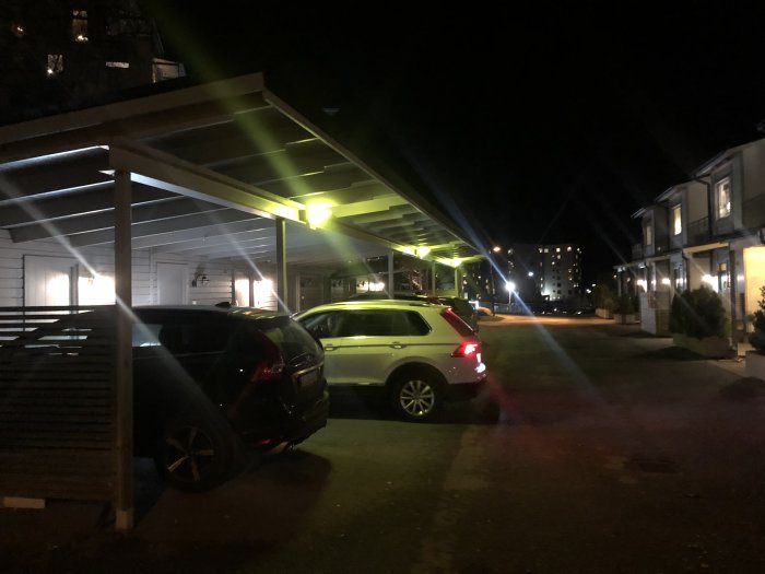 Kvällsbild av carport med bilar under svagt gröntaktig belysning från äldre lampor.