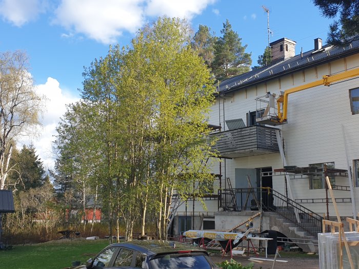 Ett hus under renovering med en skylift bredvid och byggmaterial spridda på gräsmattan.