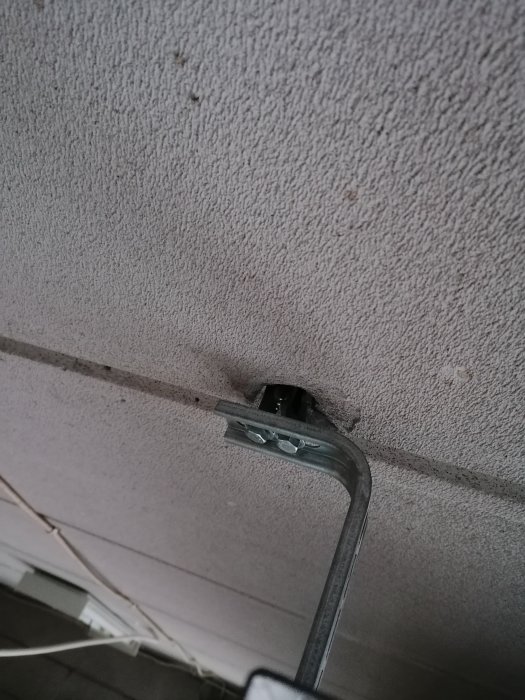 Garageportens fäste med urdragna skruvar i en vit lättbetongtak.