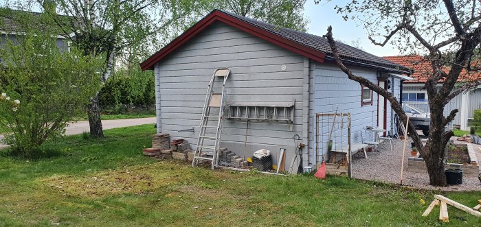 Ett hus under renovering med en stege lutad mot väggen, en hög med brukade tegelstenar och spillvirke på gräsmattan.