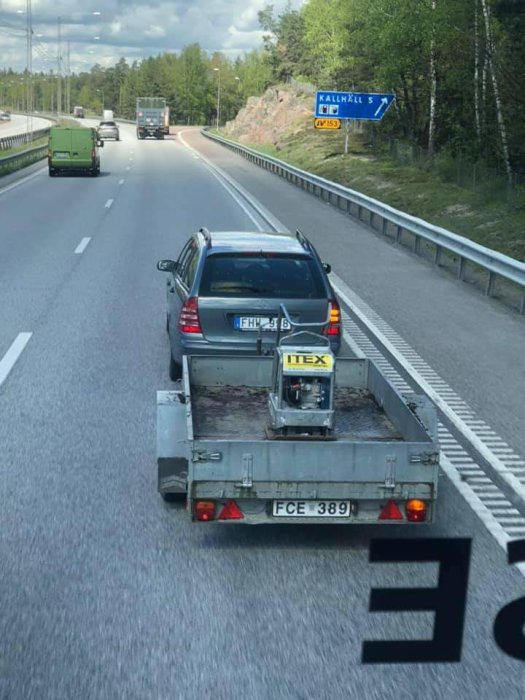 Biltransport på motorväg med personbil lastad på en släpvagn, skylt för Kallhäll i bakgrunden.