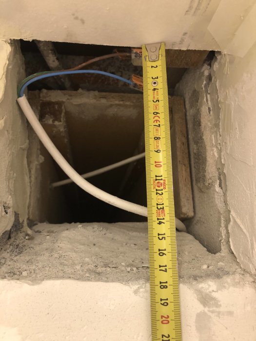 Måttband visar 12 cm avstånd vid en öppen ventilationskanal med synliga kablar i ett badrum under renovering.