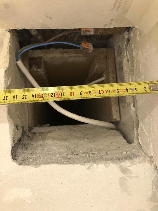 Öppet ventilationshål i badrumsvägg med måttband och elkabel.