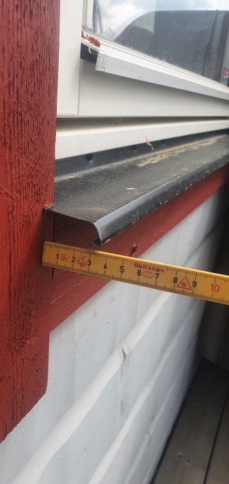 Måttband visar avståndet mellan fönsterbleck och fasad på en rödfärgad vägg.
