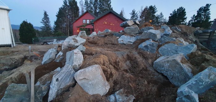 Stenar arrangerade i grävd yta för framtida 3-4 stegs vattenfall i en trädgård under konstruktion.