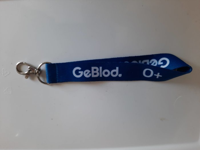 Blå nyckelband med texten "GeBlod. O+" och en karbinhake.