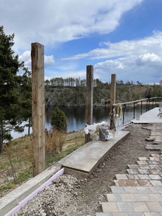 Grundläggning för utekök vid vatten med stolpar och betonggolv under uppbyggnad.