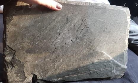 Platt skifferliknande gravsten som hålls av en hand, potentiell brist på stabilitet när den ställs upp.