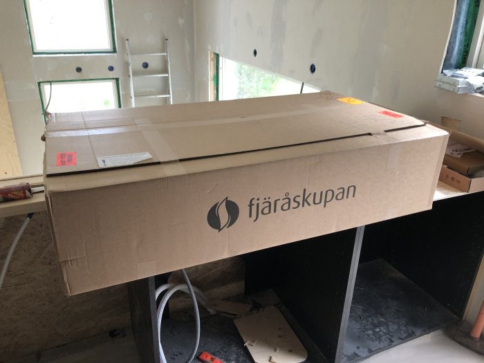 Ett stort paket för en bänkskiva placerat på en svart arbetsbänk inne i ett ofärdigt kök under renovering.