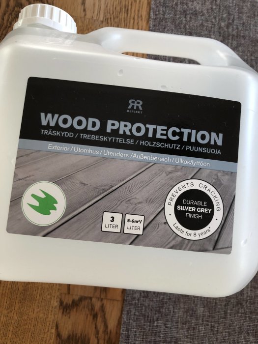 Träskyddsprodukt i vit behållare med texten "WOOD PROTECTION" och en silvergrå trall på etiketten.