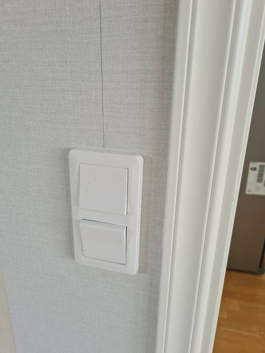 Väggmonterad dubbel elektrisk strömbrytare intill dörrfoder.