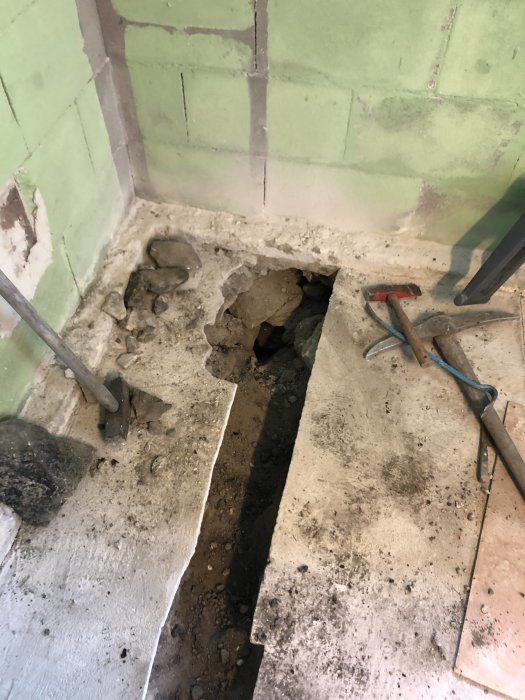 Renoveringsprojekt med utsatt rör och uppbrutet betonggolv, verktyg och byggmaterial synliga.
