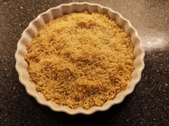 En paj med smuligt täcke i en vit pajform på grått köksbord.