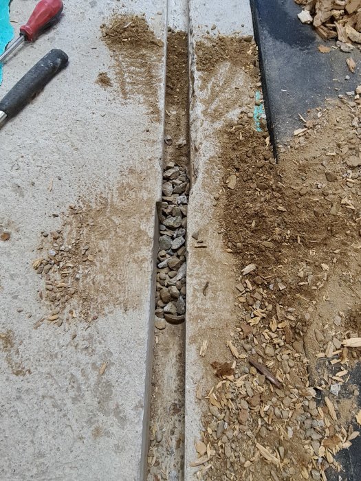 Armeringsstål med makadam och träbitar på betongyta i ett grävningsprojekt.
