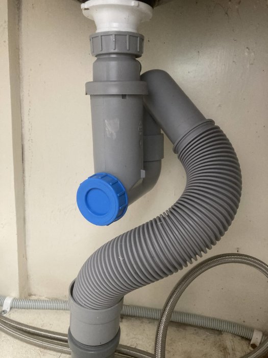 Grått vattenlås utan diskmaskinsuttag under en diskbänk, kopplat till en flexibel avloppsslang och vattenledningar.