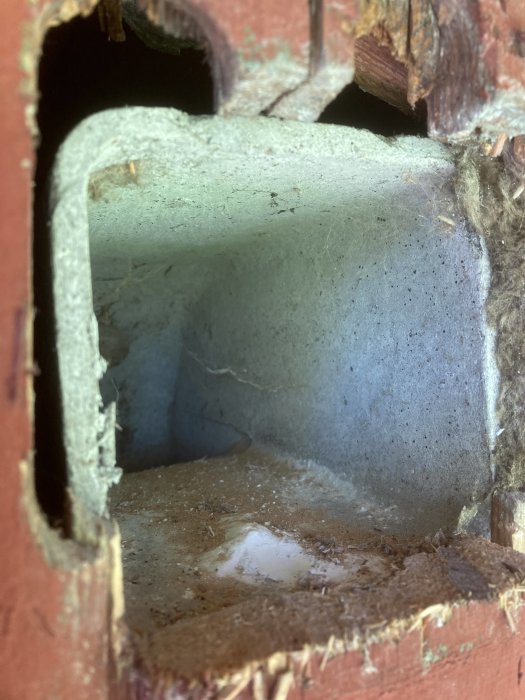 Fyrkantigt äldre utventilationsrör genom vägg med tilläggsisolering sett inifrån en sommarstuga.