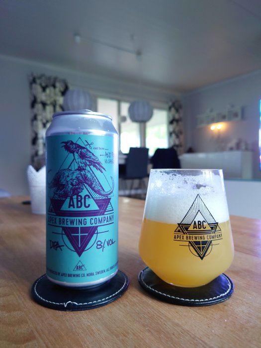 En ölburk och ett glas med öl från Apex Brewing Company på ett bord.