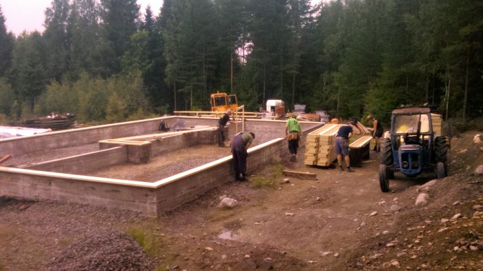 Arbetslag vid grundläggning med uteluftventilerad krypgrund och betongbalkar, byggarbetsplats i skogsmiljö.