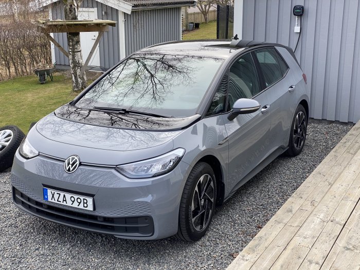 Volkswagen ID.3 parkerad bredvid laddstation på en grusuppfart.