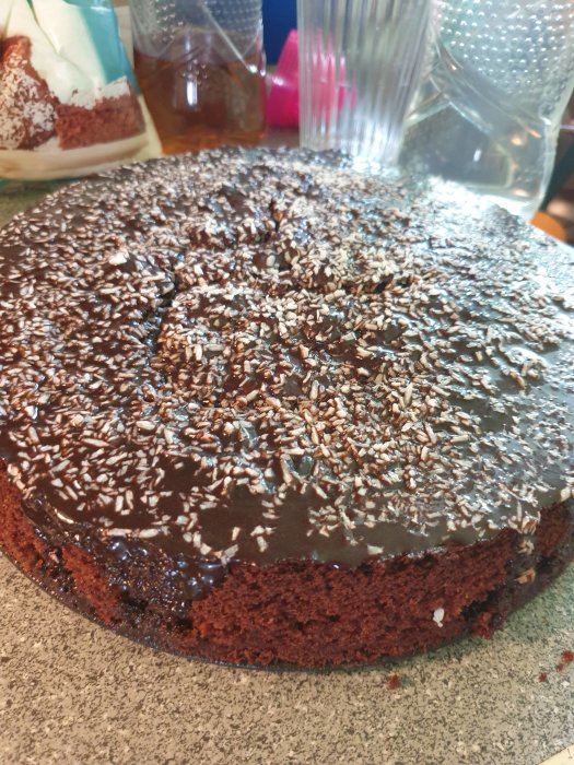 Hembakad chokladkaka med glasyr och strössel på ett köksbord.
