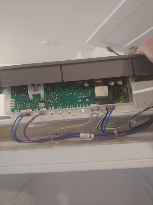 Bilden visar en öppnad elektrisk kontrollmodul med synliga brännskador och en hand som håller upp panelen.