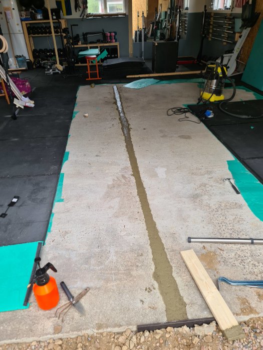Nyhälld betong längs en spricka på ett garagegolv med verktyg och skyddsmatta runtomkring.