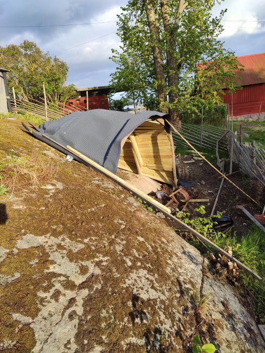 Pågående bygge av en halvrund grillplats med träväggar och tak under konstruktion intill ett berg.