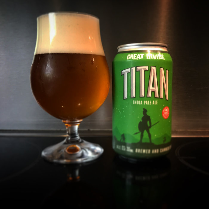 Ett glas med öl bredvid en burk Great Divide Titan India Pale Ale på en bänk.