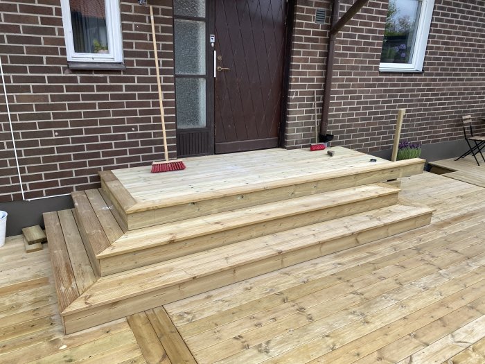 Nybyggd trätrappa utan räcke framför en husentré, redo för räcke och stuprörsomdragning.