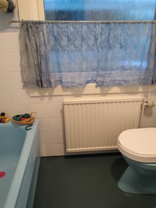 Ett daterat badrum med blåa sanitära installationer, ett väggmonterat element och ett frostbelagt fönster.