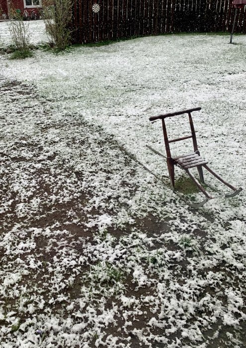 En trädgård täckt av ett tunt lager snö med en ensam trästol.