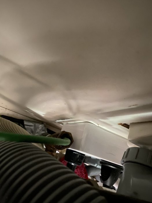 Vy under diskbänk med grön värmeslinga som går in i kallvattenledning och spår av läckage.