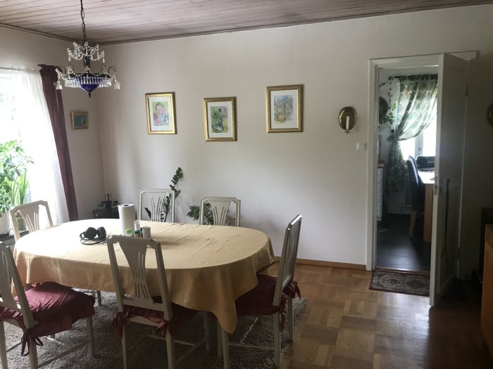 Matsal med bord klätt med gul duk, stolar med röda kuddar, kristallkrona och konst på väggarna.