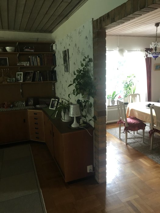 Vardagsrum med tegelvägg, trähylla med böcker, sidobord och trägolv.