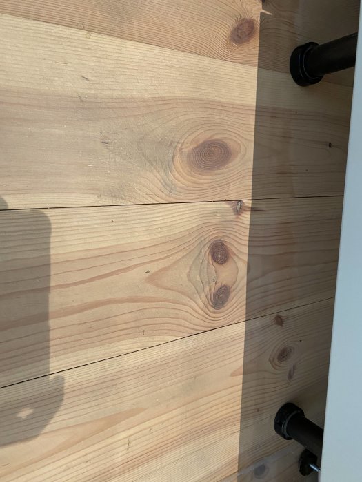 Trägolv med svullna plankor vid en diskho, golvsockel och del av rör synliga.