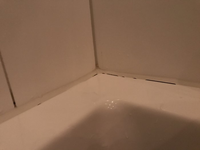 Hörnet av en dusch med vit kakel där fog behöver repareras.
