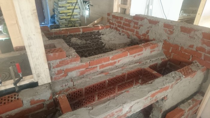 Konstruktion av en köksspis bakugn i rött tegel under byggprocessen med murbruk och verktyg synliga.