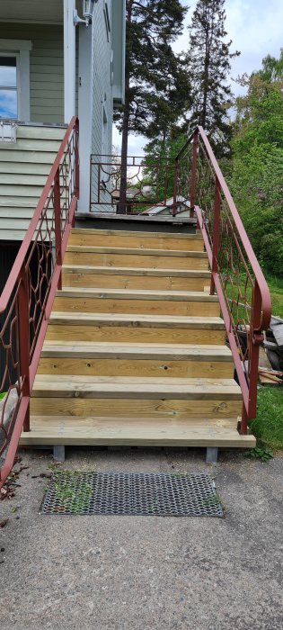 Renoverad trappa med nytt trävirke och rödmålade sidoräcken framför en husentré.