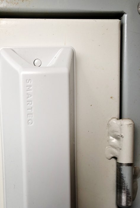 Vit antenn monterad på kanten av ett öppet elektricitetsskåp blockerar skåpdörren från att stängas ordentligt.