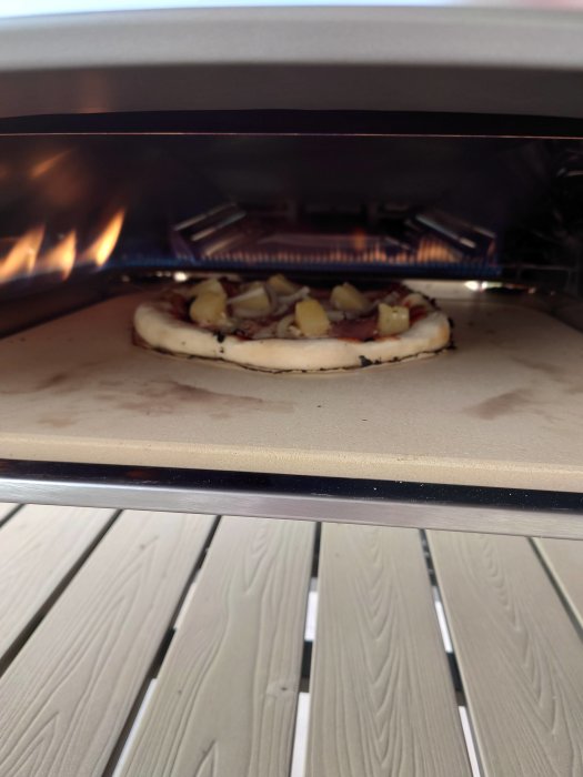 Pizza gräddas i ugn utan bakplåtspapper, med synliga lågor i bakgrunden.