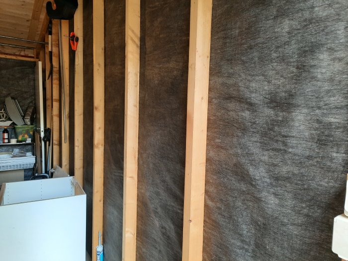 Oisolerat förråd med synliga träreglar och svart väv på väggarna.