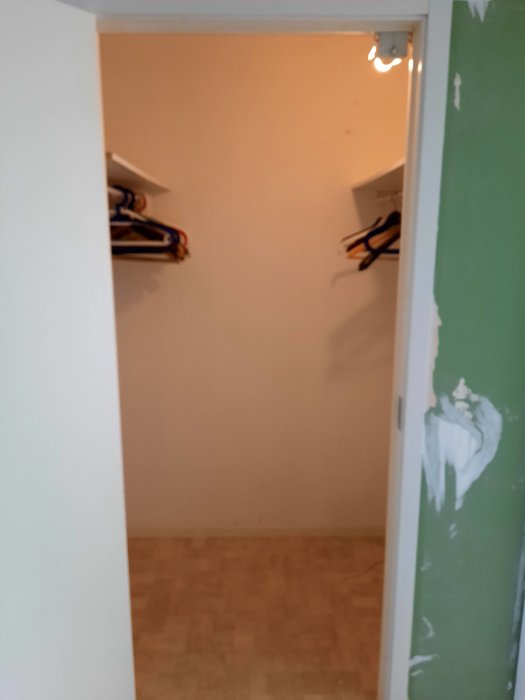 Interiör av ett oisolerat förråd med en öppen dörr och synliga reglar på en vägg.