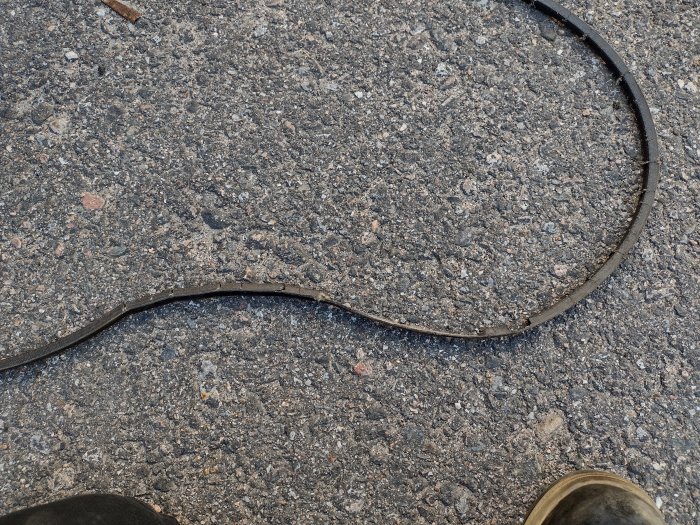 Sliten drivrem på asfaltsunderlag, trolig orsak till byte varje sommar.