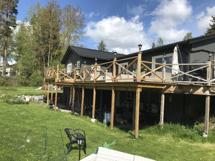 Alt: Obehandlat trästaket på en altan i anslutning till ett hus med mörkgrå panel under en solig himmel.